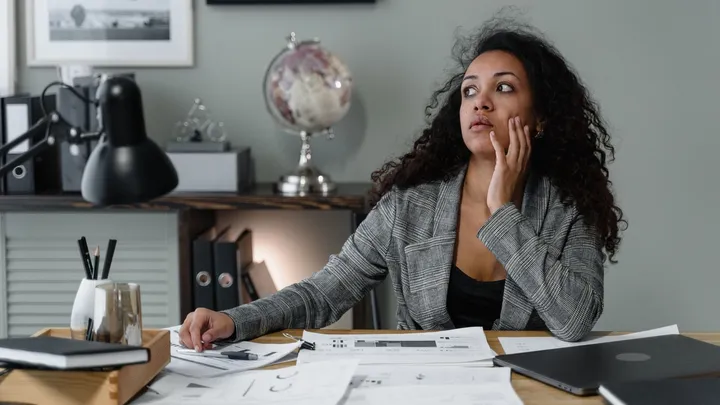 Femme d’affaires pensive à son bureau, entourée de documents