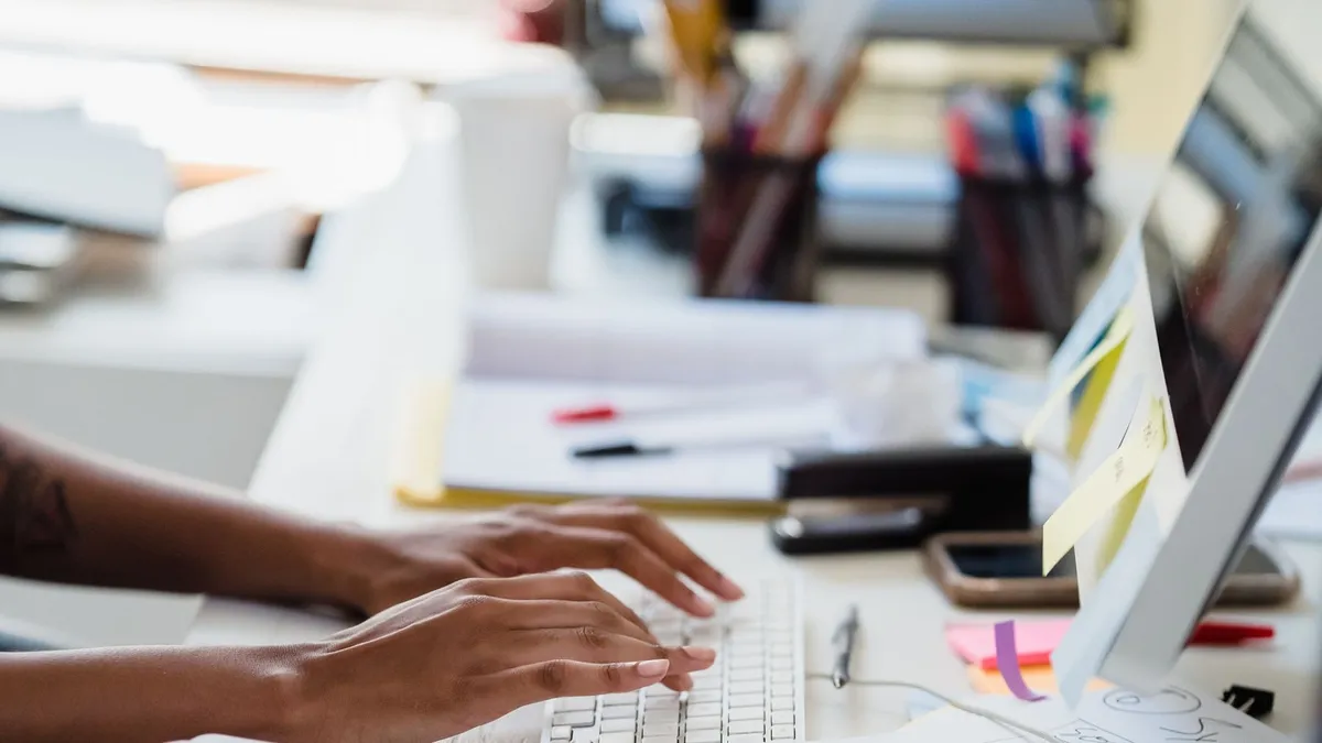 Mains tapant sur un clavier dans un bureau, écran allumé en arrière-plan